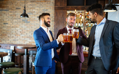 Happy young businessmen drinking beer and talking at pub after work