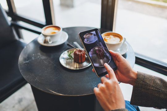 A woman using mobile phone to take a photo of coffee and snack before eat in cafe
