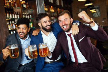 Men fans screaming and watching football on TV and drink beer in a pub