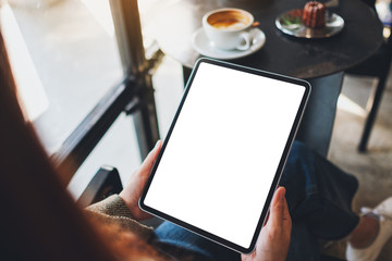 Mockup image of a woman holding black tablet pc with blank white screen in cafe