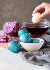 Blue marble Easter eggs painted by natural dyes. Purple cabbage and girl's hand putting an egg to a bowl with liquid