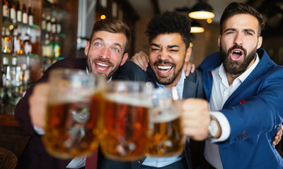 Men fans screaming and watching football on TV and drink beer in a pub