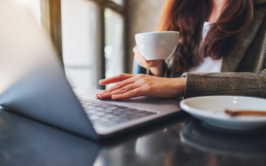 Closeup image of a woman working and touching on laptop touchpad while drinking coffee in office