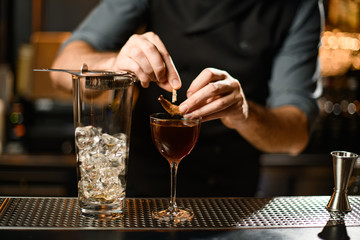 Professional bartender decorating a brown cocktail in the glass with a dried leaf by a pin
