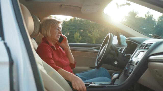 Angry senior woman sits in car uses red cell phone serious businesswoman blonde people smartphone cellphone communication internet search lady mobile bench browse network online slow motion