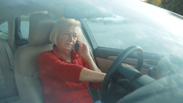 Angry senior woman sits in car uses red cell phone serious businesswoman blonde people smartphone cellphone communication internet search lady mobile bench browse network online slow motion