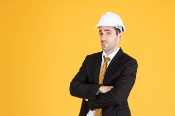 Young handsome businessman wears suit and construction helmet on isolated yellow background.