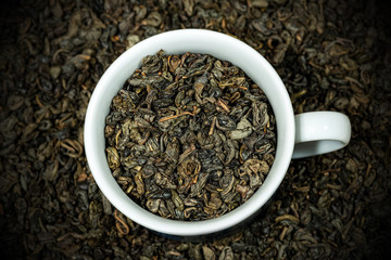 Close-up of dried leaves of green gunpowder tea in a white cup, with many rolled up leaves on the background