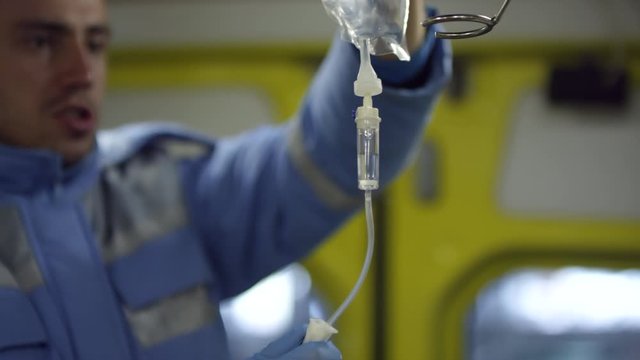 Medium shot of male paramedic preparing IV bag for patient in ambulance