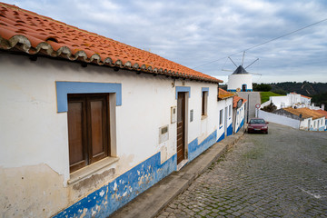 Fototapeta na wymiar Odeceixe, Portugal - Cobblestone street with blue and white traditional colorful homes and buildings in the Algarve town of Odeceixe. Windmill in background