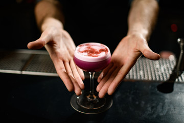 Male bartender serving a crimson alcoholic cocktail drink in the glass