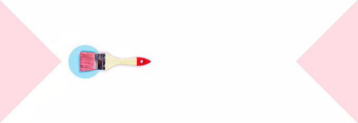 Repair concept. White and pink background with one paint brush on a paper blue circle. Flat lay, top view, copy space.