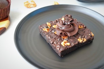 Homemade chocolate walnut brownie on dark plate garnished with chocolate ganache and walnuts. Copy space.
