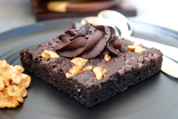 Homemade chocolate walnut brownie on dark plate garnished with chocolate ganache and walnuts. Copy space.