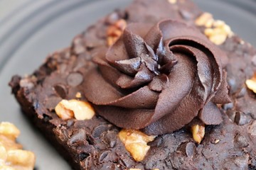 Homemade chocolate walnut brownie on dark plate garnished with chocolate ganache and walnuts. Copy space.