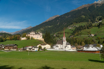 Large white stone castle and white stone Gothic Church in the Alto Adige mountains. Panoramic view from afar on an autumn sunny day