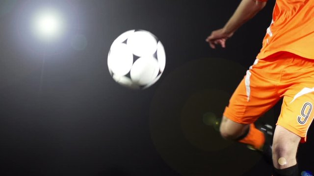 Man kicking a soccer ball / football on a Black Background. He volleys the ball past the camera. Super Slow motion
