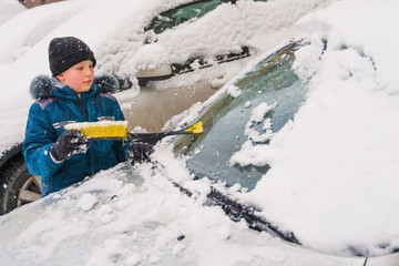 kid helps to clear the car of snow