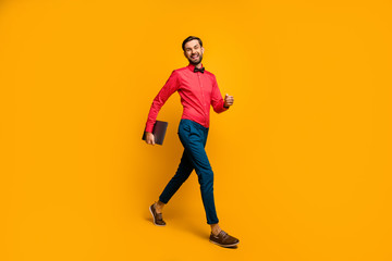 Fototapeta na wymiar Full length profile photo of macho business man walk corporate meeting training carry laptop wear stylish red shirt bow tie blue pants shoes isolated yellow color background