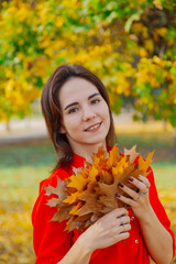 Beautiful happy woman with a bouquet of yellow leaves in autumn.