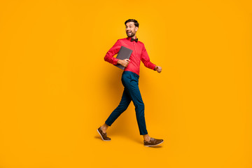 Full length profile photo of amazing business man walking corporate meeting training carry laptop wear stylish red shirt bow tie blue pants shoes isolated yellow color background