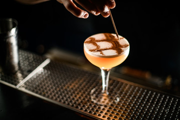 Male bartender making a pattern with the cocoa powder on the alcoholic cocktail drink in the glass
