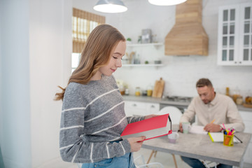 Obraz premium Long-haired girl in grey shirt standing in the kitchen wth a book