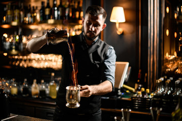 Bartender pouring a transparent alcoholic drink from the one steel cup to another