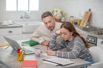 Long-haired girl in grey shirt and her father doing lessons together