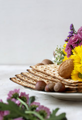 Pesah celebration concept (Jewish Passover holiday) design with wine, matzo, flowers, and nuts on white background with copy space