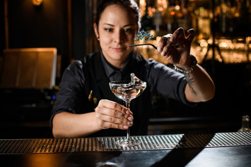 Professional bartender girl decorating an alcoholic cocktail in the glass with a dried flower by tweezers