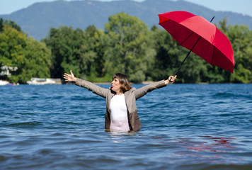 Elegant Business Woman with Suit Standing in the Water and Holding a Red Umbrella.