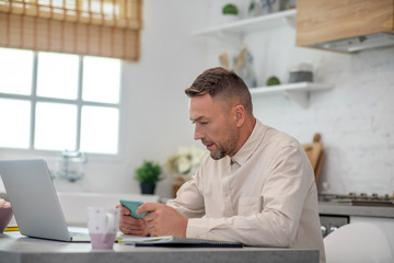 Good-looking bearded man sitting in the kitchen and typing a message