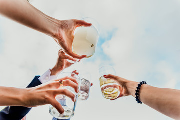 Group of friends toasting with a few glasses of alcohol with the sky in the background, seen from...