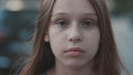 Fototapeta premium Shot from above pretty little girl with green eyes. Portrait of lovely teenager giving screw loose sign. Outdoors. Blurred background of way.