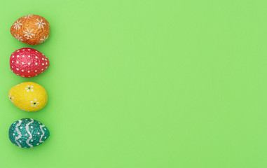 Colorful painted orange, blue, red and yellow Easter eggs on green background. Happy Easter holiday concept. Flat lay style with copy space.