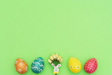 Colorful painted orange, blue, red and yellow Easter eggs with Easter rabbit and yellow spring flowers on green background. Happy Easter holiday concept. Flat lay style with copy space.