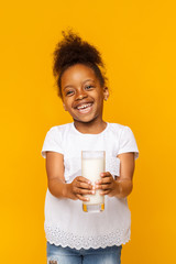 Smiling black little girl holding glass of milk