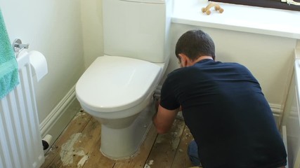 Plumber / Handyman fixing a toilet in a bathroom. The tradesman is using his tools in the repair / installation. Tilt Shot - Stock Video clip footage