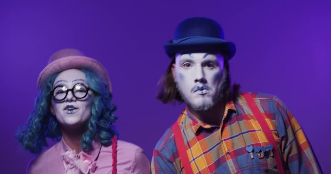 A beautiful colorful pair of funny clown mimes performing emotional synchronously dance on isolated purple background. Positive success