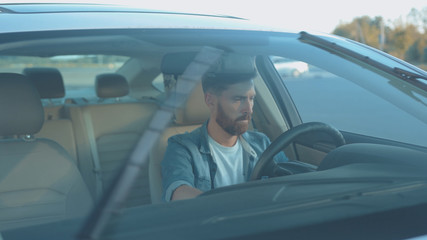 Portrait of sexy male driver steering wheel sitting in the car looking with confidence expecting adventuros roadtrip at sunset.