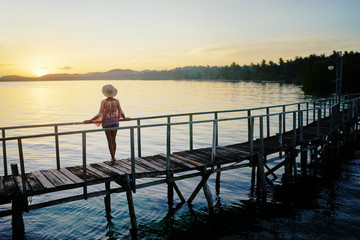 Vacation on tropical island.  Back view of young woman in hat enjoying sunset sea view from wooden bridge terrace, Siargao Philippines.