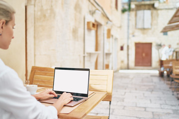 Technology and travel. Working outdoors. Freelance concept. Copy space on the screen. Close up of  young woman using laptop in sidewalk cafe on ancient europian street.