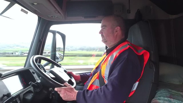 Trucking - Male Truck driver driving a Lorry on the roads. The man is sat in the cab at the steering wheel