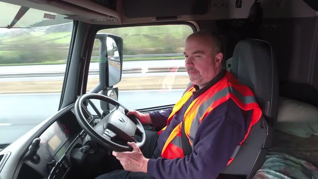 Male Truck driver driving a Lorry on the roads. The man is sat in the cab at the steering wheel
