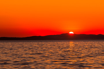 Beautiful orange sunset over the sea with sun on the mountains horizon, view from beach in Zadar, Dalmatia, Croatia, Europe