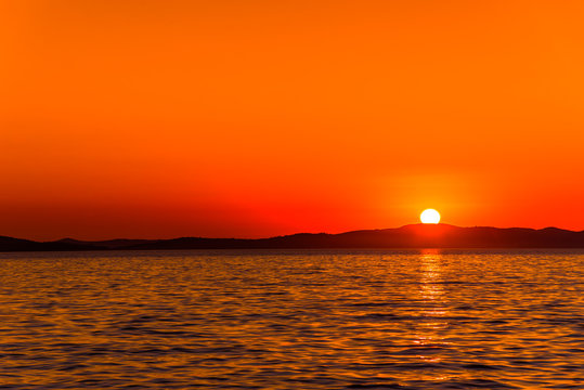 Background with landscape of sunset over sea with sun on the mountains horizon, Zadar, Dalmatia, Croatia