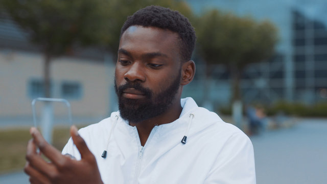 Smiling african american man uses futuristic glass phone walk at city look at camera smile nanosmartphone transparent electronic future global information innovation interface touch web slow motion - Powered by Adobe