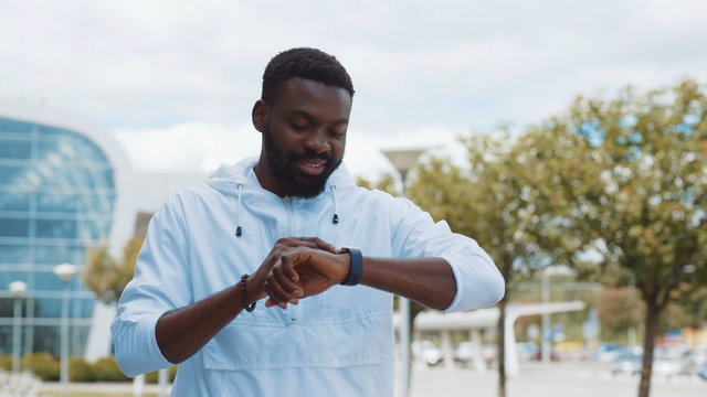 Smiling young african american man use smartwatch stand street business shopping internet face technology call texting mobile smart attractive cell communication portrait close up slow motion