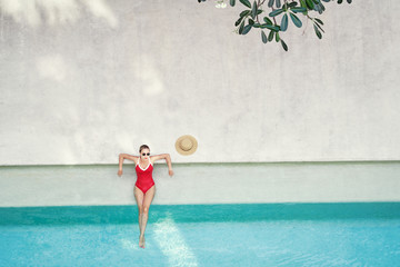 Enjoying suntan. Vacation concept. Top view of slim young woman in red swimsuit in the swimming pool.